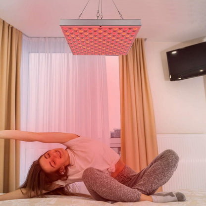 Woman stretching on a bed under a ceiling-hung red light therapy panel in a bright bedroom