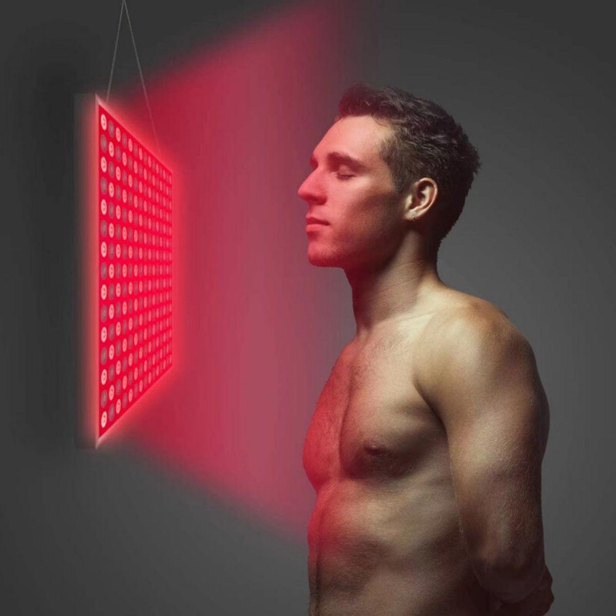 Man standing in front of a hanging red light therapy panel glowing red